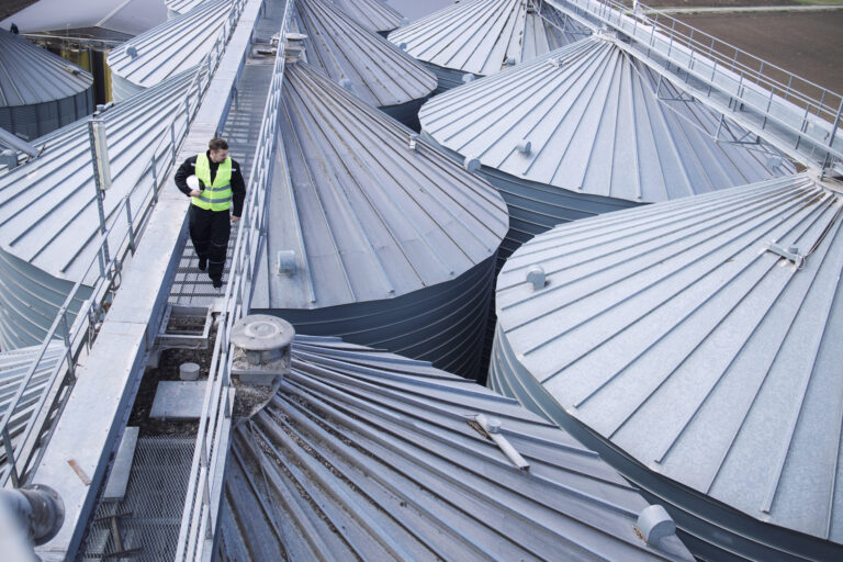 Factory worker walking on metal platform and doing visual inspection on industrial food storage tanks or silos